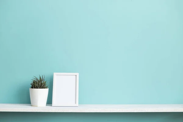 Resim çerçevesi mockup ile modern oda dekorasyonu. Saksı lı sulu bitki ile pastel turkuaz duvara karşı beyaz raf.