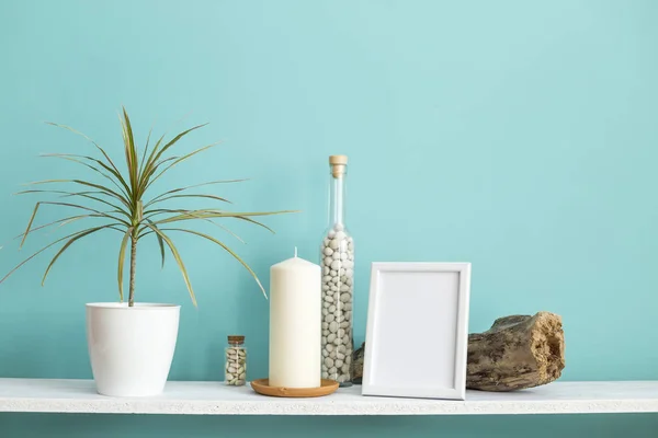 사진 프레임 모형과 현대적인 방 장식입니다. 파스텔 청록색 벽에 촛불과 바위가 있는 흰색 선반. 화분에 심은 드라카엔 식물 — 스톡 사진