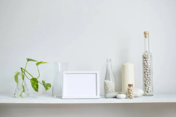 Estante contra pared blanca con vela decorativa, vidrio y rocas. esquejes de plantas en vidrio . — Foto de Stock