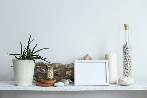 Shelf against white wall with decorative candle, glass, wood and rocks. Home plant in pot.