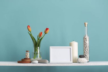 resim çerçevesi mockup. Dekoratif mum, cam ve kayalar ile turkuaz duvara karşı Raf. Vazoda laleler.