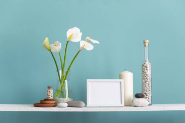 resim çerçevesi mockup. Dekoratif mum, cam ve kayalar ile turkuaz duvara karşı Raf. Vazoda Calla.