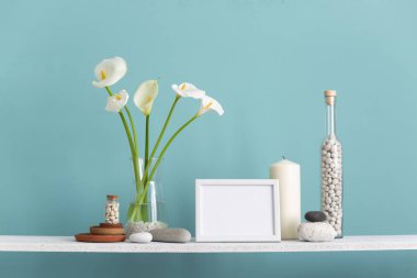 resim çerçevesi mockup. Dekoratif mum, cam ve kayalar ile turkuaz duvara karşı Raf. Vazoda Calla.