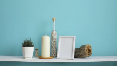 Resim çerçevesi mockup ile modern oda dekorasyonu. Mum ve şişe kayalar ile pastel turkuaz duvara karşı beyaz raf. El sulama saksı sulu bitki
