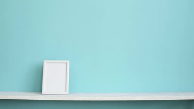 Resim çerçevesi mockup ile modern oda dekorasyonu. Saksıyılan bitkisi aşağı koyarak el ile pastel turkuaz duvara karşı beyaz raf.