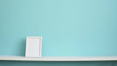 Resim çerçevesi mockup ile modern oda dekorasyonu. El saksı sulu bitki aşağı koyarak pastel turkuaz duvara karşı beyaz raf.