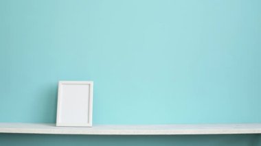 Resim çerçevesi mockup ile modern oda dekorasyonu. El saksı sulu bitki aşağı koyarak pastel turkuaz duvara karşı beyaz raf.