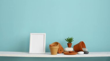 Resim çerçevesi mockup ile modern oda dekorasyonu. Çanak çömlek ve etli bitki ile pastel turkuaz duvara karşı beyaz raf. El saksı sulu bitki aşağı koyarak.