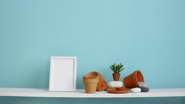 図フレームモックアップ付きのモダンな客室の装飾 陶器とジューシーな植物とパステルターコイズの壁に対する白い棚 鉢植えの多肉植物を置く手 — ストック動画