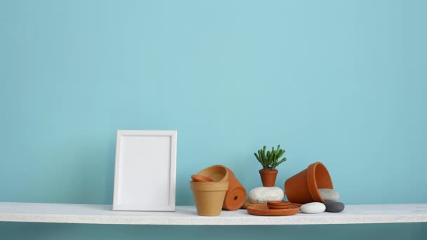 図フレームモックアップ付きのモダンな客室の装飾 陶器とジューシーな植物とパステルターコイズの壁に対する白い棚 鉢植えサボテンを置く手 — ストック動画