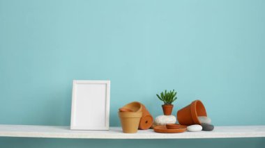 Resim çerçevesi mockup ile modern oda dekorasyonu. Çanak çömlek ve etli bitki ile pastel turkuaz duvara karşı beyaz raf. Saksılı örümcek bitkisi aşağı koyarak El.