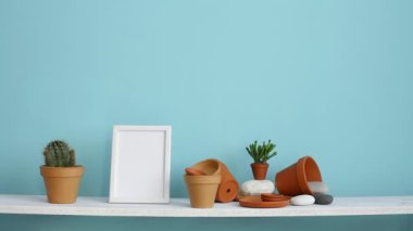 Resim çerçevesi mockup ile modern oda dekorasyonu. Çanak çömlek ve etli bitki ile pastel turkuaz duvara karşı beyaz raf. El sulama saksı kaktüs bitki.
