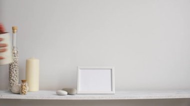 Resim çerçevesi mockup ile modern oda dekorasyonu. Dekoratif mum, cam ve kayalar ile beyaz duvara karşı Raf. Saksı lı kaktüs bitkisi koyarak el.
