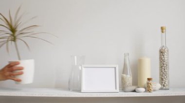Resim çerçevesi mockup ile modern oda dekorasyonu. Dekoratif mum, cam ve kayalar ile beyaz duvara karşı Raf. El saksı dracaena bitki aşağı koyarak.