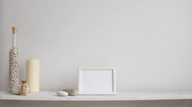 Resim çerçevesi mockup ile modern oda dekorasyonu. Dekoratif mum, cam ve kayalar ile beyaz duvara karşı Raf. El saksı sulu bitki aşağı koyarak.