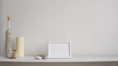 Resim çerçevesi mockup ile modern oda dekorasyonu. Dekoratif mum, cam ve kayalar ile beyaz duvara karşı Raf. El saksı sulu bitki aşağı koyarak.