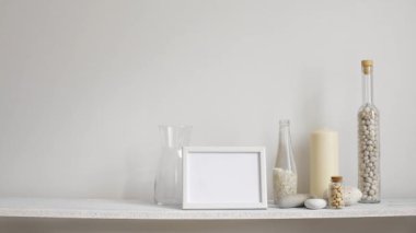 Resim çerçevesi mockup ile modern oda dekorasyonu. Dekoratif mum, cam ve kayalar ile beyaz duvara karşı Raf. El saksı sulu bitki aşağı koyarak.