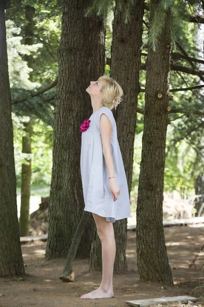松の木の下に立っている間、明るいドレスを着た美しい裸足の若い女性の完全な長さの肖像画 — ストック写真