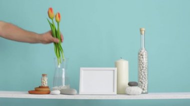 Resim çerçevesi mockup ile modern oda dekorasyonu. Dekoratif mum, cam ve kayalar ile turkuaz duvara karşı Raf. El vazo lale koyarak.