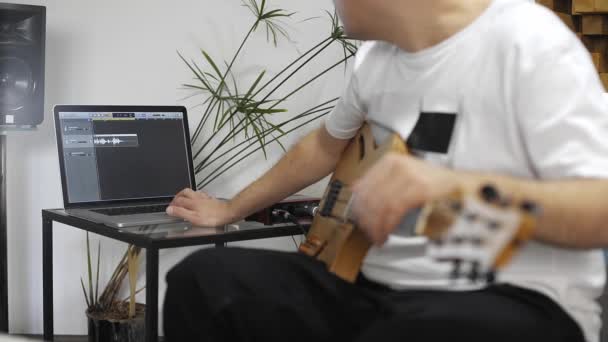 自宅のデジタルスタジオでエレキギターを録音するプロのミュージシャンのクローズアップ 彼は楽器とミディコントローラーに囲まれています 音楽制作コンセプト — ストック動画