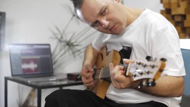自宅のデジタルスタジオでエレキギターを録音するプロのミュージシャンのクローズアップ 彼は楽器とミディコントローラーに囲まれています 音楽制作コンセプト — ストック動画