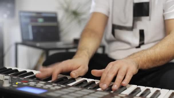 自宅のデジタルスタジオでミディキーボードを記録するプロのミュージシャンのクローズアップ 彼は楽器とミディコントローラーに囲まれています 音楽制作コンセプト — ストック動画