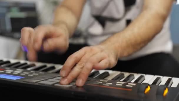 自宅のデジタルスタジオでミディキーボードを記録するプロのミュージシャンのクローズアップ 彼は楽器とミディコントローラーに囲まれています 音楽制作コンセプト — ストック動画