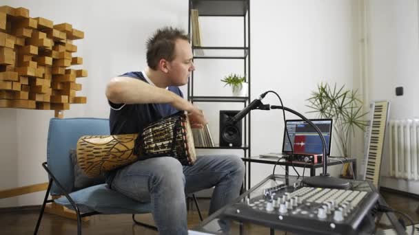 プロのミュージシャンは 自宅のデジタルスタジオでジャンベドラム楽器を録音します 彼は楽器とミディコントローラーに囲まれています 音楽制作コンセプト — ストック動画