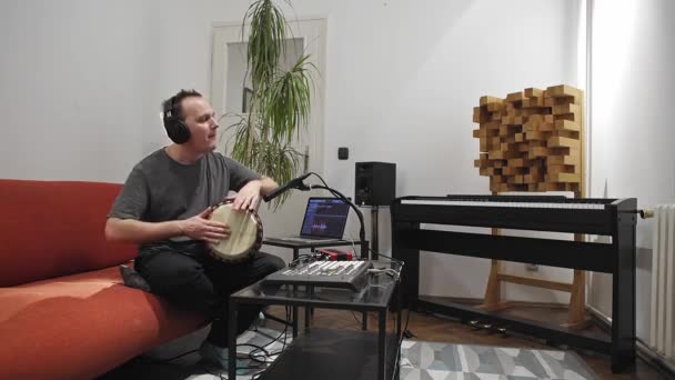 プロのミュージシャンは 自宅のデジタルスタジオでジャンベドラム楽器を録音します 彼は楽器とミディコントローラーに囲まれています 音楽制作コンセプト — ストック動画