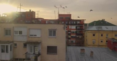İnsansız hava aracı, Novi Sad şehir merkezinde ki eski binanın yanında yavaşça yükselirken, güvercin sürüsü etrafta uçarken muhteşem gün batımına bakıyor. 