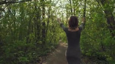Gri bir elbisenin içinde genç çekici kadın, baharda kalın bir ormana giden yol boyunca geziniyor. Kadın eşyaları güneş gözlüğü ve güzel hava sahiptir.