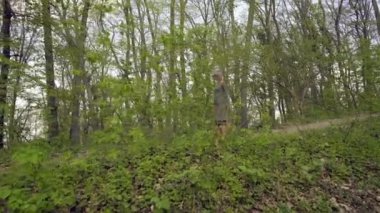 Gri bir elbisenin içinde genç çekici kadın, baharda kalın bir ormana giden yol boyunca geziniyor. Kadın eşyaları güneş gözlüğü ve güzel hava sahiptir.