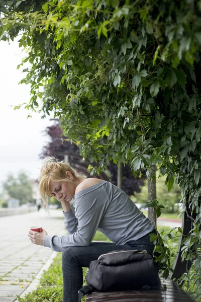 公園に座り、コーヒーを飲み、悲しげに考える女性の肖像画. — ストック写真