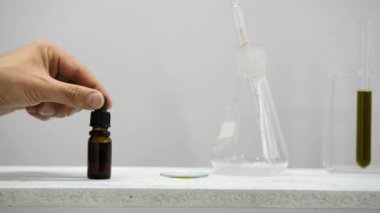 CBD ile cam tüplere sahip duvara beyaz raf. el damlalar ile saat cam üzerinde CBD yağı bırakarak. Orada saksı esrar bitki var. Sağlık konsepti.