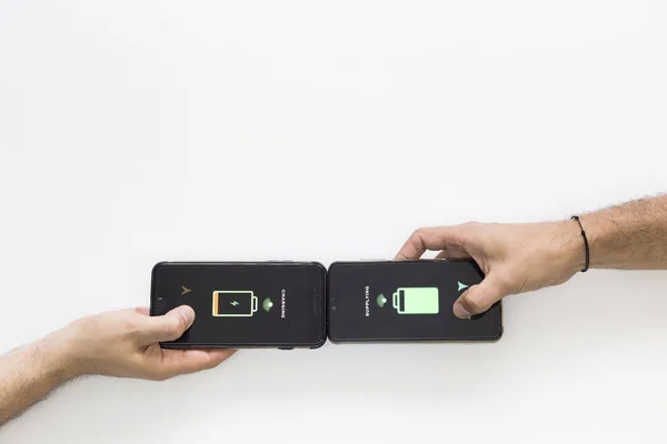 Two hands holding black smart phones while they are wireless charging.