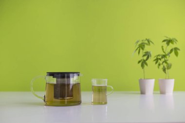 Çömlekçilikte marihuana bitkisi olan beyaz masa. Bardakta ve çaydanlıkta sıcak Cbd çayı.