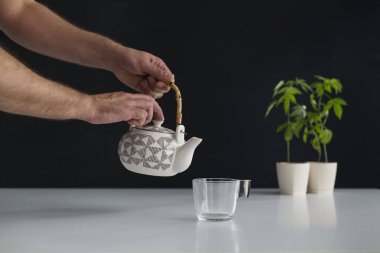 Çömlek içinde esrar bitki ile beyaz masa. Cam için sıcak CBD çayı dökmek el.