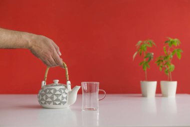 Çömlek içinde esrar bitki ile beyaz masa. Cam için sıcak CBD çayı dökmek el.