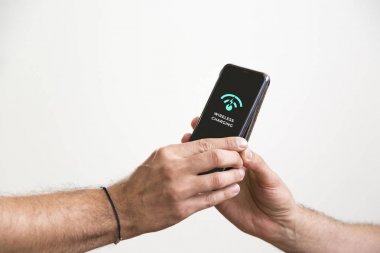 Kablosuz şarj olurken iki el Siyah akıllı telefonlar tutarak.