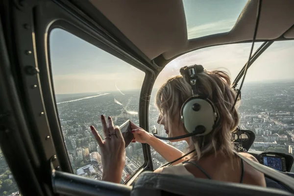 Güzel sarışın kadın helikopterde akıllı telefon ile cityscape fotoğraf çekmek.