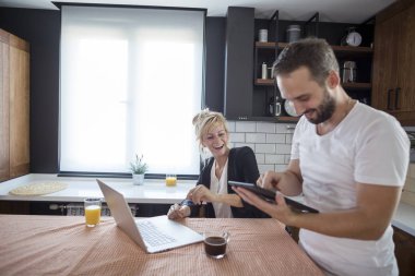 Sabah mutfakta bir çift. Onlar gülümsüyor ve tablet ve dizüstü bilgisayar tarama.