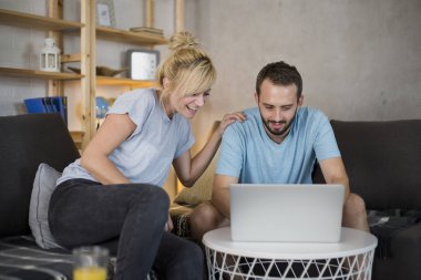 Modern oturma odasında kanepede oturan çift. Eğleniyorlar, dizüstü bilgisayar izliyorlar..