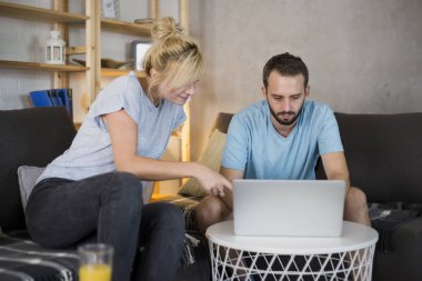 Modern oturma odasında kanepede oturan çift. Eğleniyorlar, dizüstü bilgisayar izliyorlar..