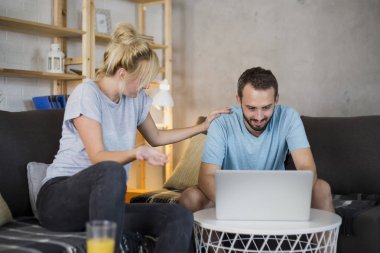 Modern oturma odasında kanepede oturan çift. Eğleniyorlar, dizüstü bilgisayar izliyorlar..