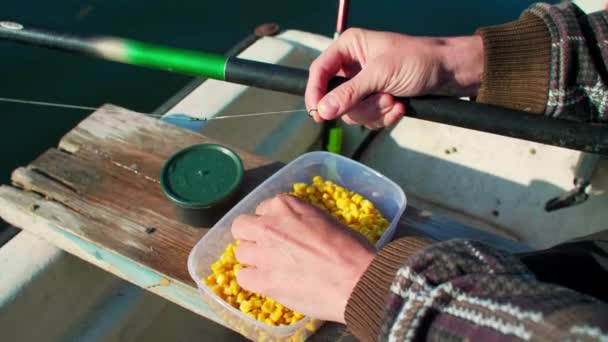 釣りのフックに餌としてトウモロコシを設定する手を閉じる 男は釣り竿を持っていて シンカーで並んでいる 川に浮かぶ船の中で働いている — ストック動画
