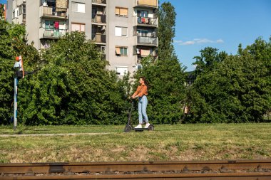 Genç ve güzel bir kız arka planda eski binalar olan bir yerleşim yerinden elektrikli scooter ile geçiyor..