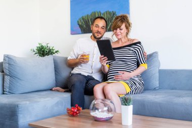 Genç ve mutlu bir evli çift oturma odasında kanepede oturmuş tablet izliyor..