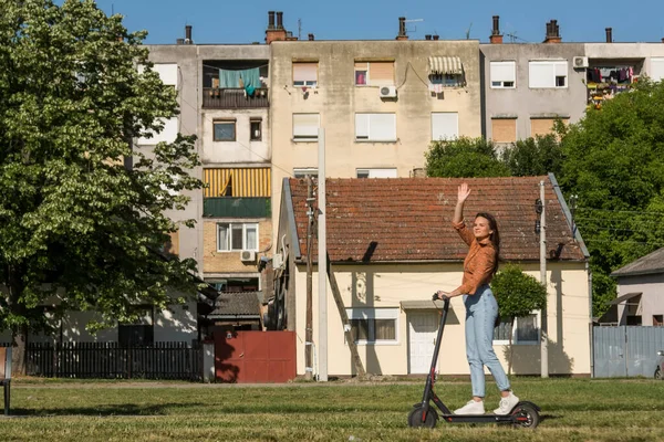 아름다운 여성이 도시의 스쿠터를 가면서 사진사의 방향으로 흔들고 있습니다 — 스톡 사진