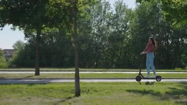 年轻美丽的女人骑着电动车穿过公园和绿色的环境 在一些镜头中 她的头发被风吹散了 — 图库视频影像