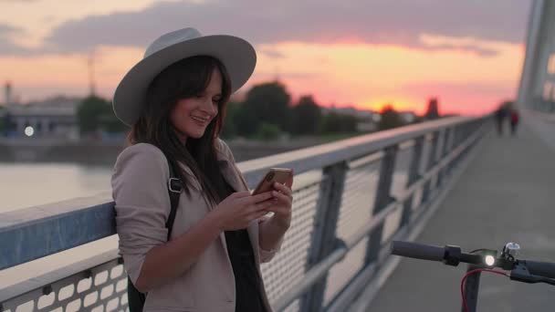 Młoda Uśmiechnięta Kobieta Opiera Się Ogrodzenie Mostowe Pisze Telefonie Obok — Wideo stockowe